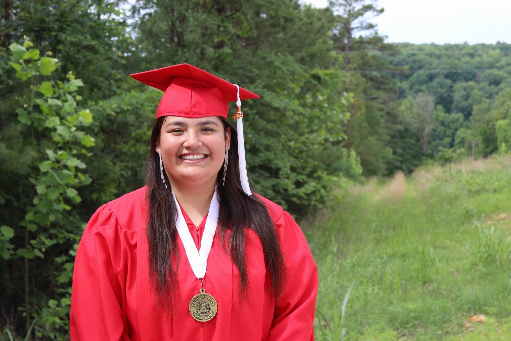 Ahbrianna smiling in a red graduation cap and gown with a salutatorian medal at her Cookson Hills graduation